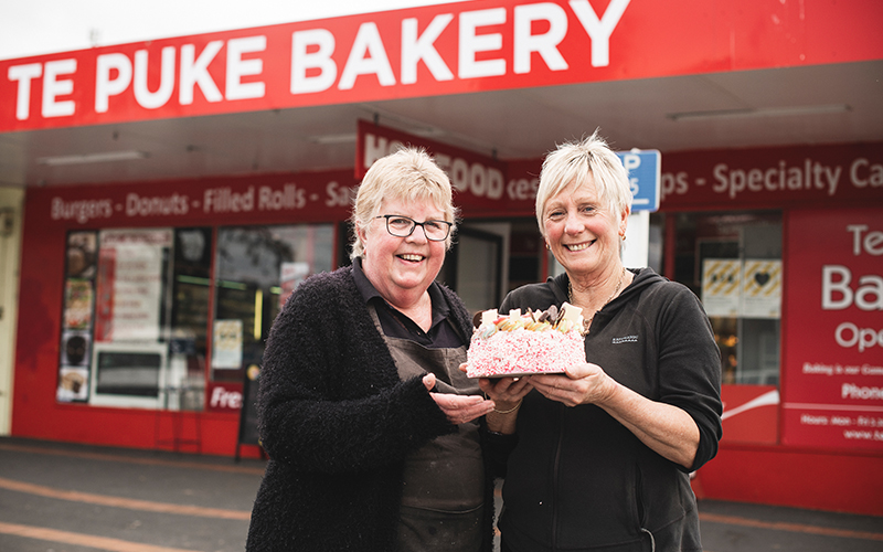 Julie and Silvia hold a cake in front of Te Puke Bakery