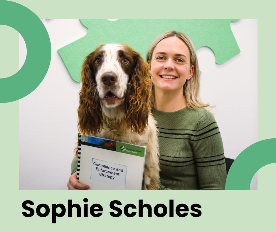 Western Bay staff member Sophie Scholes posing with a dog on her lap and a copy of the Compliance Strategy